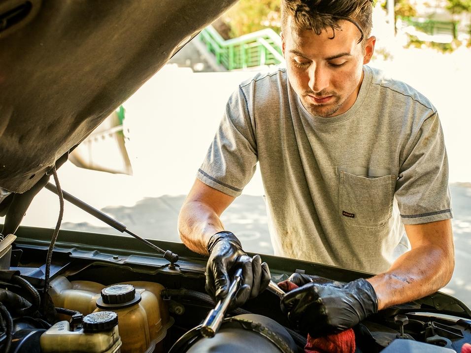 Automotive Departyment | Man Working on Vehicle with black latex gloves on and grease all over him with a tan tshirt on